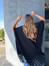 Ruana negra tejida en lana con aplique de cuero en la espalda y flecos en el ruedo.
