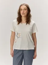 Remera negra de manga corta con cuello redondo y detalle de bordado floral en tono tostado en la parte inferior derecha.