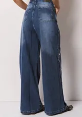 Pantalón de jean azul de corte wide leg, con diseño de botones metálicos a presión a lo largo de las costuras laterales. Presenta un lavado localizado y tiro alto.