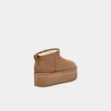 Botas de caña baja tipo botineta con plataforma elevada, confeccionadas en gamuza color marrón. Presentan costuras con detalle de puntada overlock, lengüeta trasera y forro interior de lana suave.