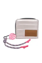 Billetera pequeña acolchada color rosa pálido metalizado, con cierre de cremallera. Presenta un parche de cuero marrón con texto grabado y un accesorio colgante con cordón estampado en tonos rosa y azul marino.