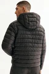 Campera puffer liviana negra con cuello elevado y capucha, cierre frontal con protección para el mentón, bolsillos laterales con cierre y bolsillos interiores abiertos. Tiene un corte ajustado que realza la silueta.