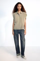 Camisa fluida de cuello solapa y manga corta, con diseño a rayas en tonos beige y blanco, detalle de pliegues en los hombros y cierre frontal con botones.