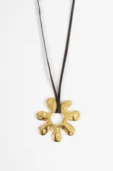 Collar largo con cordón de gamuza sintética en color negro y dije central de metal dorado con forma de flor orgánica de diseño irregular.