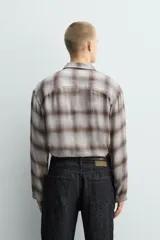 Camisa relaxed fit de manga larga con cuello solapa, confeccionada en tejido con mezcla de viscosa. Presenta un bolsillo plastrón en el pecho, bajo con aberturas laterales y cierre frontal de botonadura. El diseño es a cuadros en tonos beige y marrón.