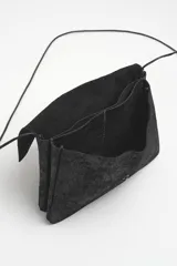Bandolera pequeña de cuero negro con acabado laminado, diseño tipo sobre con cierre de broche a presión y correa de cuero fina extraíble.