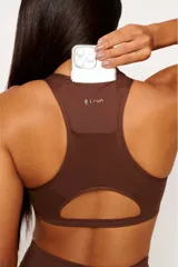 Top deportivo de espalda nadadora con diseño ergonómico, color marrón. Cuenta con un bolsillo integrado en la parte superior de la espalda y una abertura inferior, confeccionado en tejido técnico de alta compresión con detalles reflectivos.