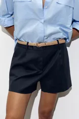 Bermuda de tiro medio color azul marino, con pinzas delanteras, cierre frontal y cinturón fino color beige.