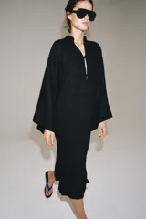 Vestido túnica largo negro de corte midi con mezcla de viscosa y lino, escote en V y mangas largas evasé. Presenta cierre frontal con alamares decorativos.