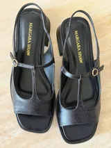 Sandalia de gamuza color marrón, con diseño tipo T-strap, taco cuadrado bajo y tira ajustable al talón con hebilla metálica dorada.