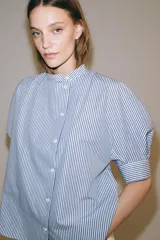 Camisa de algodón con estampado de rayas verticales azules y blancas. Presenta cuello mao, cierre frontal con botones a contraste y mangas cortas abullonadas con puños rectos.