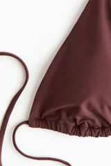 Top de bikini triangular color marrón con copas con relleno extraíble, tiras ajustables para atar al cuello y en la espalda.