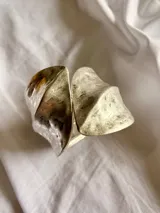 Brazalete rígido de diseño abierto, acabado en tono plateado con textura martillada y forma curva.