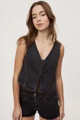 Chaleco corto de denim negro con escote en V y diseño sin mangas. Presenta terminación lavada y detalles laterales con entramado y tachas metálicas que aportan un toque distintivo.