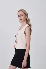 Chaleco de lino y viscosa color natural, con escote en V y cierre frontal mediante lazos con cuentas de madera.