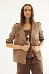 Chaqueta corta de inspiración motoquera color beige, confeccionada en lino fantasía, sin forro, con cierres decorativos, broches de presión y bolsillos delanteros funcionales. Presenta detalle bajo el cuello y en vueltas de mangas en color mostaza y rayas.