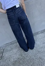 Pantalón jean azul oscuro, de corte wide leg y tiro medio. Presenta detalles de costuras diagonales en la parte superior.