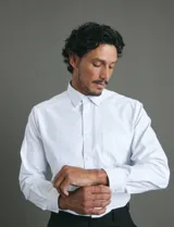 Camisa de vestir blanca de manga larga, con cuello clásico, cierre frontal de botones y bolsillo en el pecho.