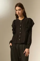 Camisa negra de viscosa con textura arrugada, cuello a la base y cierre frontal con botones. Presenta volados en los hombros y mangas largas.