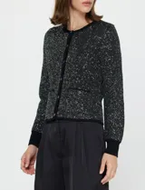 Cardigan de manga larga marca Current Air, confeccionado en tejido con lentejuelas bordadas en color negro. Presenta cuello redondo, cierre frontal con botones metálicos y bolsillos delanteros. Los puños, el cuello y el bajo están terminados en punto elástico negro.