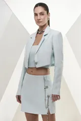 Blazer de corte cropped en color celeste pastel, con solapas clásicas, cierre frontal de un botón metálico decorativo y mangas largas. Presenta un diseño sastrero estructurado y forro interior.