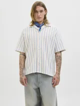 Camisa de manga corta estilo resort, confeccionada en tejido jersey de punto con diseño de rayas verticales en tonos crudo y azul. Presenta cuello camisero y cierre frontal con botones.