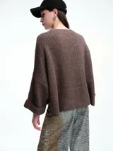 Sweater de tejido de punto color marrón con textura tipo waffle, diseño amplio, hombros caídos y cuello redondo. Presenta un bolsillo frontal aplicado y mangas con puños anchos decorados con botones.