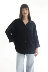 Camisa negra de pana, corte oversize, con cuello camisero, cierre frontal con botones, dos bolsillos con solapa en el pecho y mangas largas con puños abotonados.