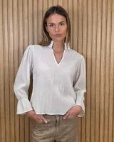 Blusa blanca de algodón con escote en V y cuello mao. Presenta mangas largas abullonadas con puños acampanados y fruncidos.