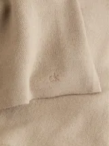 Sweater color beige de lana con escote en v, mangas largas y hombros caídos. Presenta logo de Calvin Klein en la parte superior trasera.