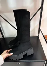 Botas bucaneras de color negro con caña alta confeccionada en tela elástica tipo gamuza y suela track de goma gruesa.