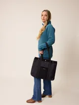 Bolso tipo tote de diseño acolchado con patrón de rombos, confeccionado en poliamida negra. Presenta un bolsillo frontal central de pana con el logo de la marca bordado en dorado, detalles de ribetes en pana negra y botones metálicos dorados en la parte superior. Incluye correas de hombro resistentes y forro interior de algodón a cuadros.