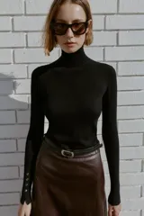 Jersey de punto liso en color beige, con cuello alto y manga larga con detalle de botones metálicos en los puños.