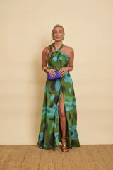 Vestido largo de satén con estampado abstracto en tonos verdes y azules, escote halter con nudo en el cuello, falda evasé y una abertura frontal pronunciada en la pierna.