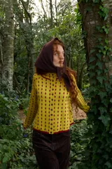 Cardigan reversible de punto con diseño de rombos pequeños, cuello redondo y cierre frontal con botones. Presenta un patrón de rombos en color rojo sobre fondo amarillo, con terminaciones en color rojo.
