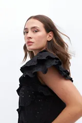 Vestido midi de lino blanco con diseño de broderie, cuello alto, cierre frontal con botones y volados decorativos en los hombros y el cuerpo.