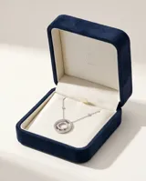 Collar de acero con cadena fina que presenta pequeños apliques de circonias a lo largo de su extensión. El dije central tiene un diseño circular doble, con el borde exterior pavé de circonias y tres pequeñas piedras rojas incrustadas en la parte inferior del círculo interior.