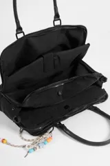 Briefcase negro de nylon con tres compartimentos, dos con cierre, bolsillo delantero con solapa y cierre de broche a presión. Cuenta con doble asa de mano, correa regulable y un llavero decorativo con cuentas coloridas colgando de uno de los herrajes.