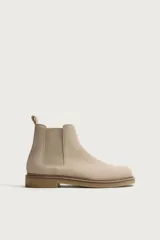 Bota Chelsea de hombre en color beige, confeccionada en piel con acabado serraje. Cuenta con elásticos laterales, trabilla trasera para facilitar el calce y suela plana con ligero tacón.