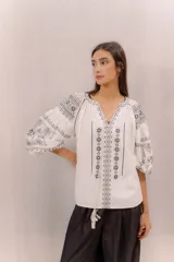 Blusa blanca con bordados en contraste de estilo bohemio, mangas amplias y diseño ligero.