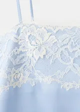 Vestido corto de tejido satinado color celeste, con diseño recto, escote recto y tirantes finos. Presenta detalles de encaje blanco en el escote y en el ruedo.