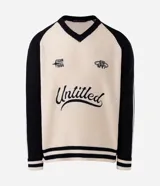 Suéter de punto con corte boxy, diseño bicolor en crema y negro. Presenta cuello en V, mangas largas con rayas laterales y estampa frontal con lettering Untitled y detalles gráficos. Cuenta con terminaciones acanaladas a rayas en el ruedo y puños.