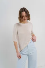 Buzo de tejido abierto color beige claro, de calce oversize con mangas 3/4 y cuello redondo. Presenta terminaciones acanaladas en puños y cintura.