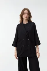 Blazer negro de corte recto y holgado, con doble botonadura frontal, solapas clásicas y mangas tres cuartos con costuras pespunteadas en contraste.