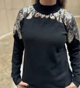 Buzo color crudo de mangas largas con apliques de lentejuelas plateadas y doradas en los hombros.