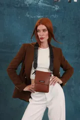 Phonebag pequeña color mostaza, confeccionada en cuero sintético, con solapa frontal y correa ajustable con logo de la marca.