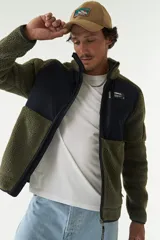 Campera de sherpa con paneles en contraste de color azul marino en el pecho y cuello alto. Cuenta con cierre frontal completo, bolsillos laterales y un bolsillo frontal con cierre, confeccionada en tejido de poliéster.