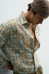 Camisa de corte relajado confeccionada en tejido fluido con estampado geométrico en tonos azules y ocres. Presenta cuello solapa, cierre frontal de botones y manga larga con puños abotonados.