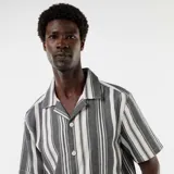 Camisa de manga corta con cuello solapa y cierre frontal de botones, con diseño de rayas verticales en tonos negro y blanco.