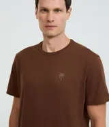 Remera de corte comfort, color marrón, con cuello redondo, manga corta y estampa localizada de palmera en el pecho.